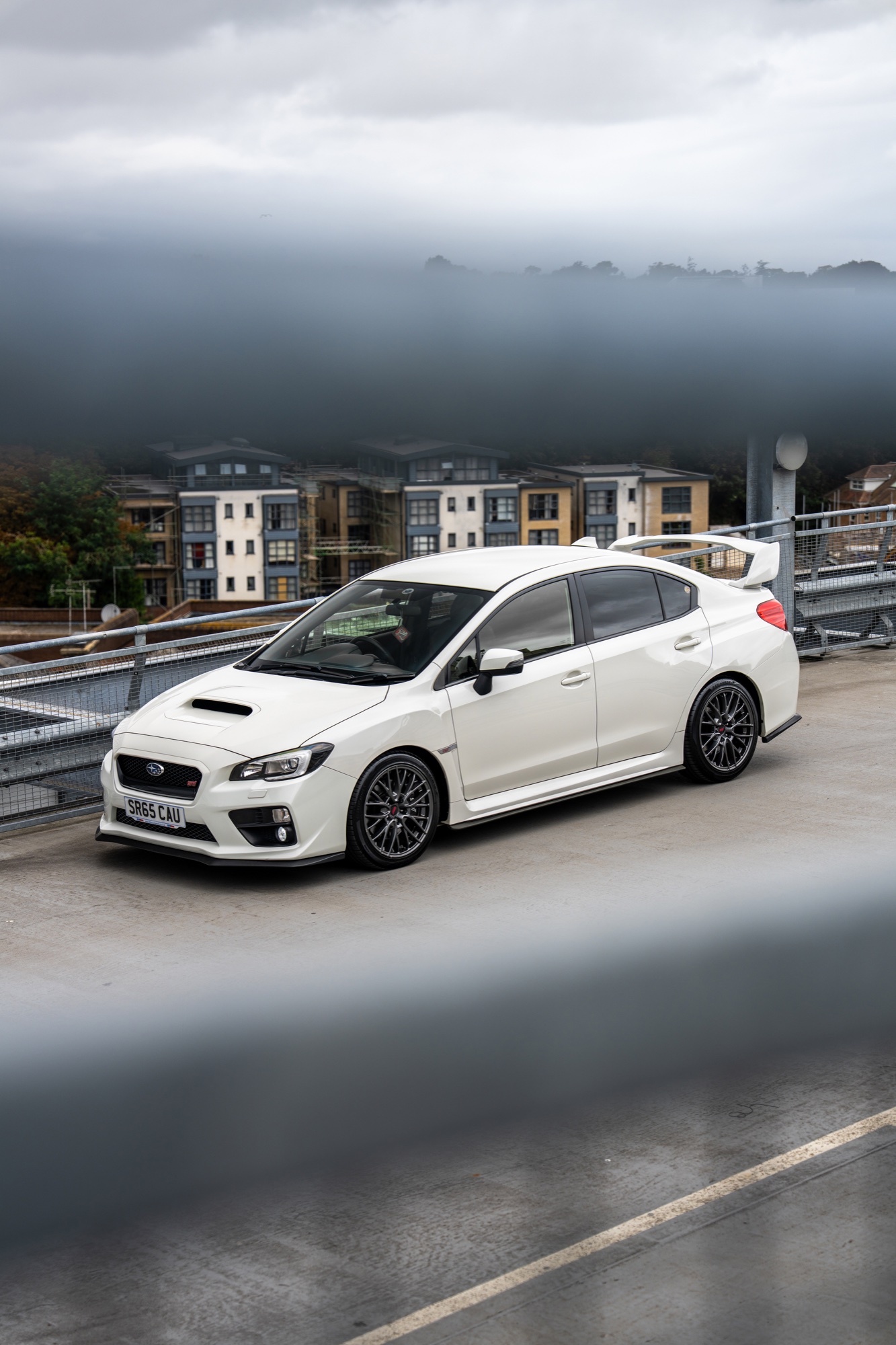 White performance car photographed beneath atmospheric low cloud